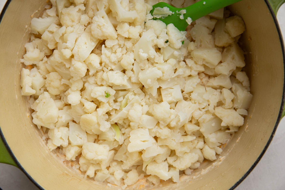 Steamed cauliflower florets in a large pot with creamy sauce, ready to be stirred together.