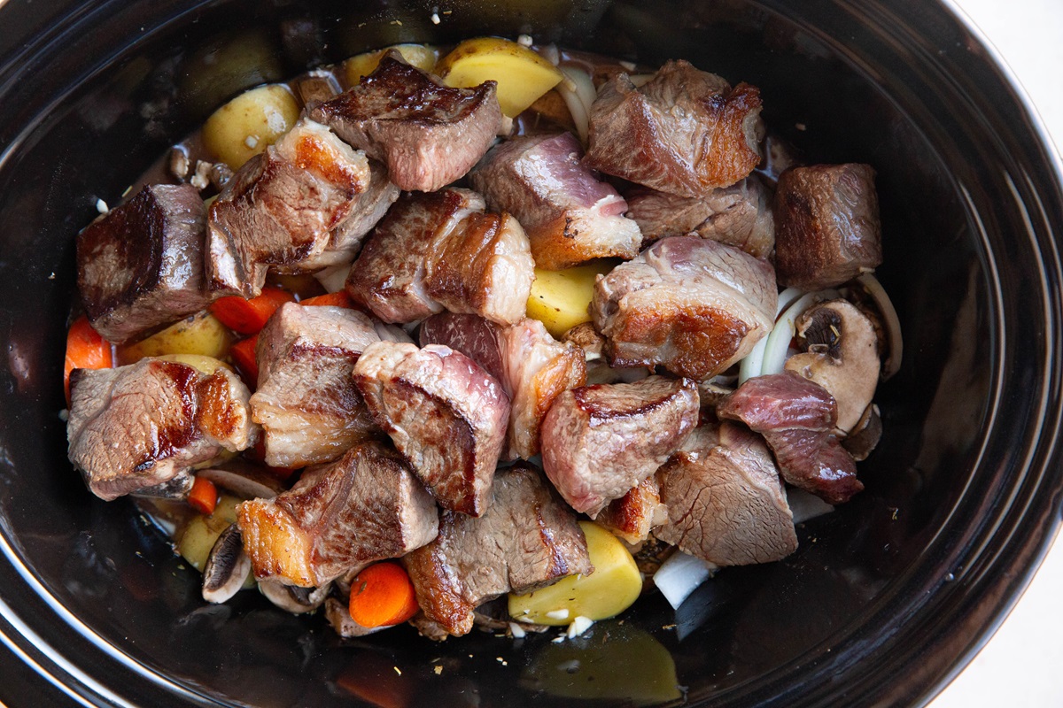 Seared beef chunks on top of vegetables in a slow cooker, ready to make beef stew.