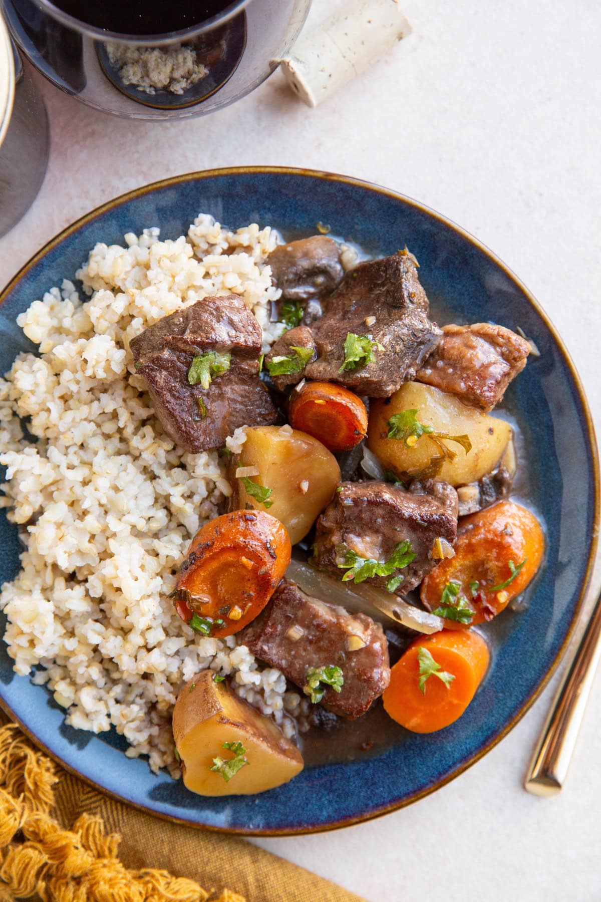 Blue plate with French beef stew, brown rice, and a glass of red wine.