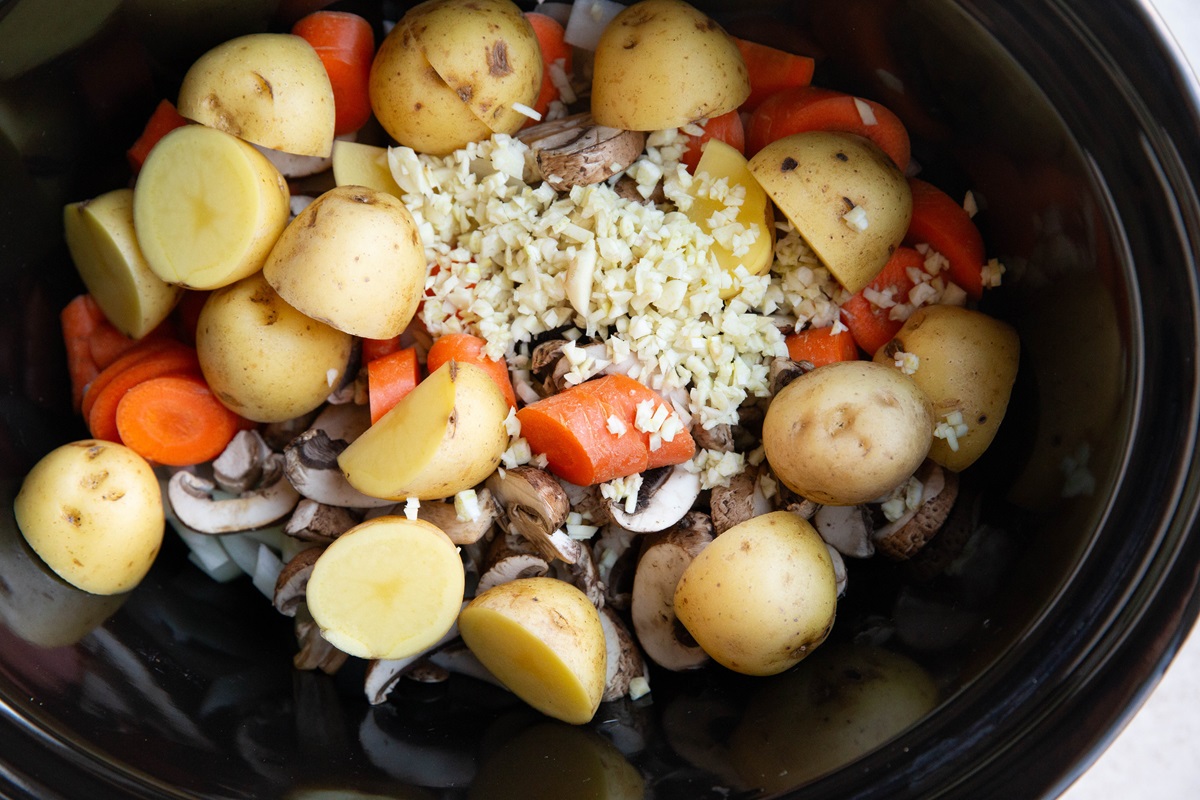 Onions, mushrooms, potatoes, carrots, and garlic in a slow cooker to make French stew.