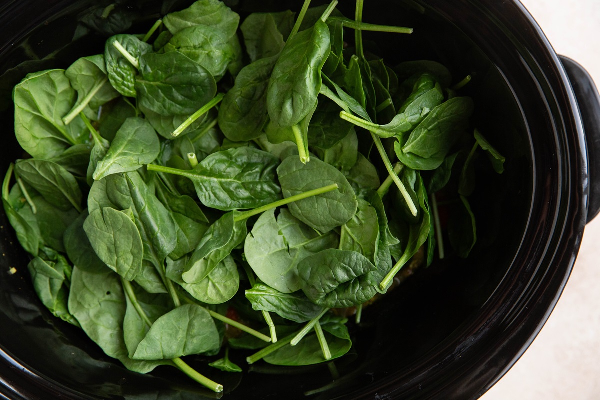 Spinach in a crock pot, ready to be mixed into soup.