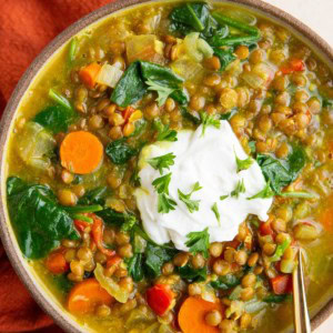 Bowl of curry lentil soup with Greek yogurt on top and a red napkin to the side.