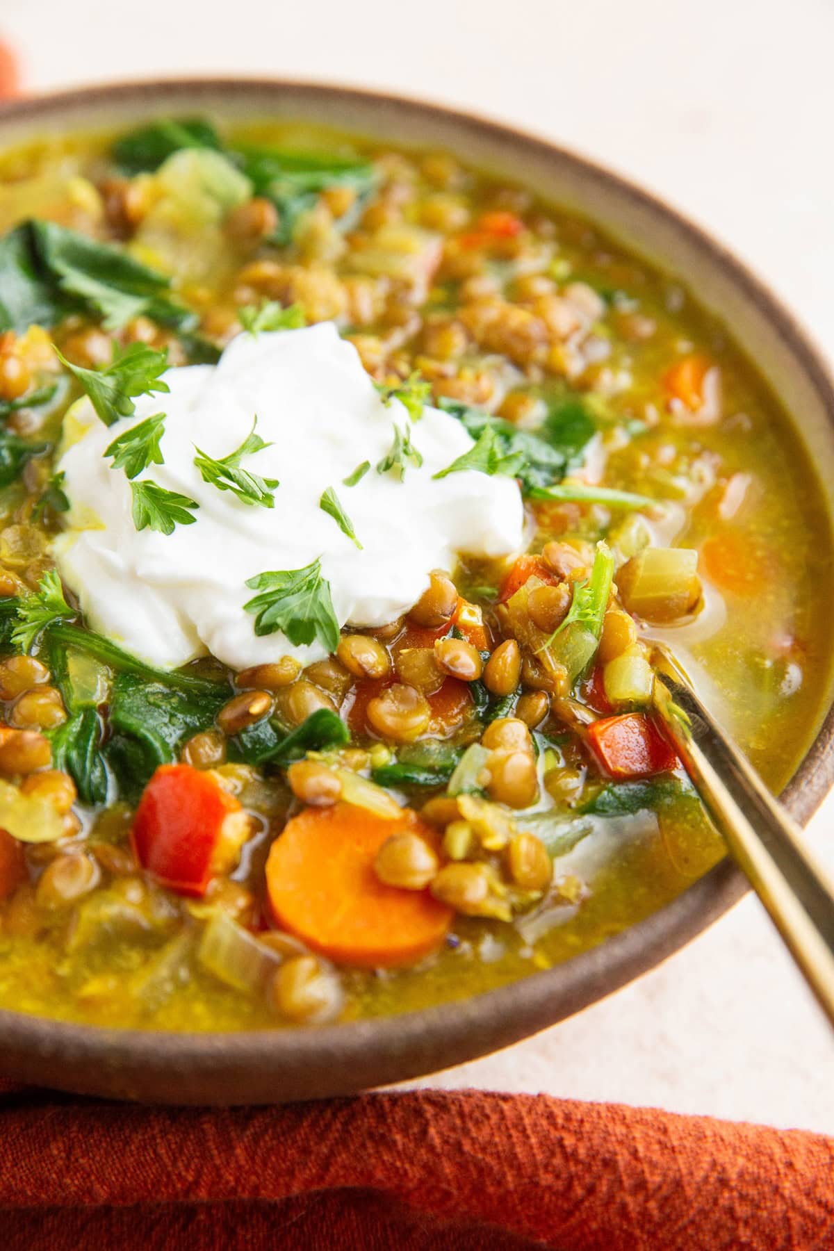 Ceramic Bowl of curry lentil soup with Greek yogurt on top and a red napkin to the side and a golden spoon.