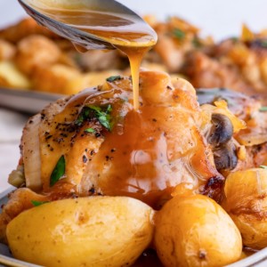 Spoon drizzling sauce over chicken and potatoes.