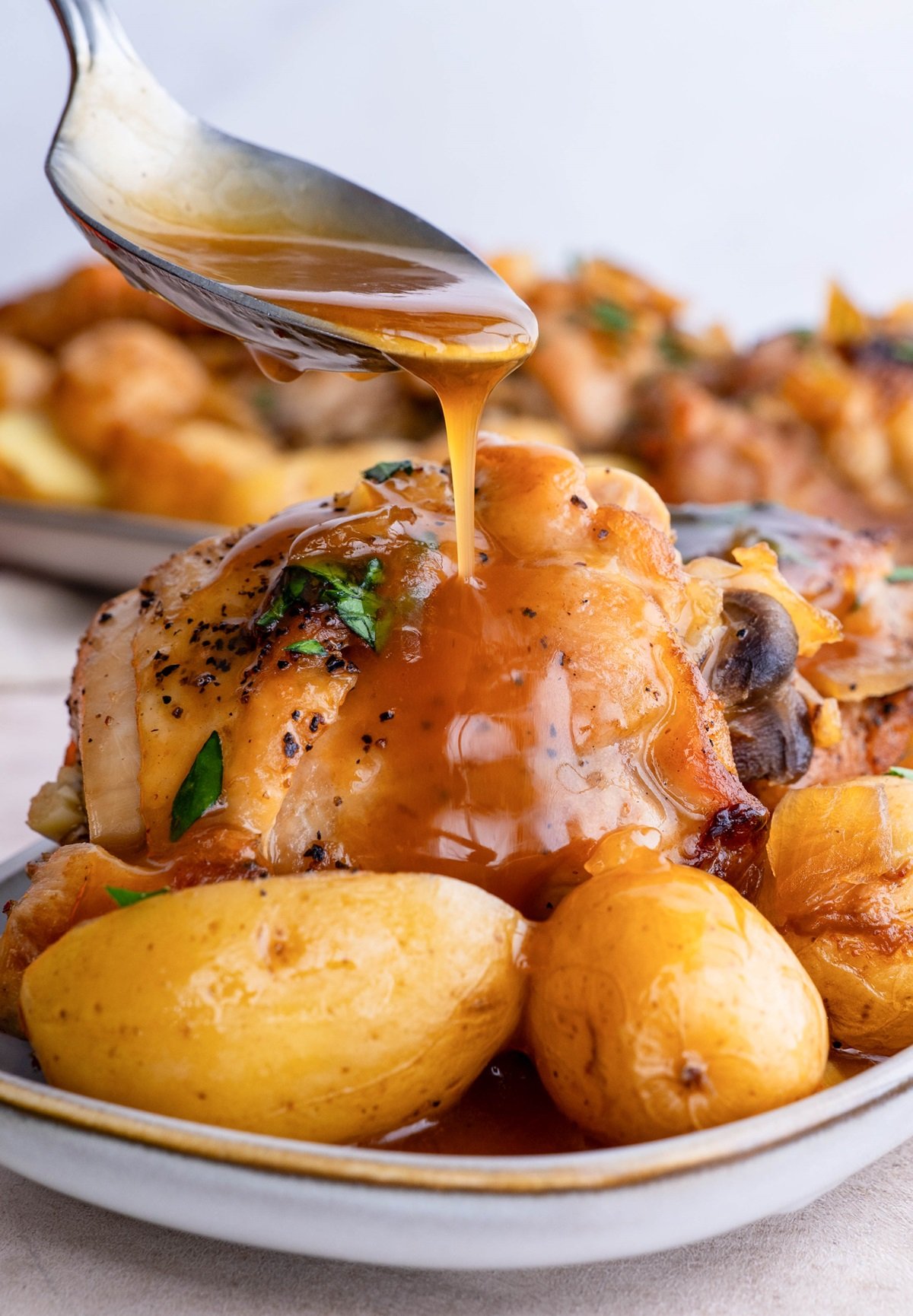 Spoon drizzling sauce over chicken and potatoes.