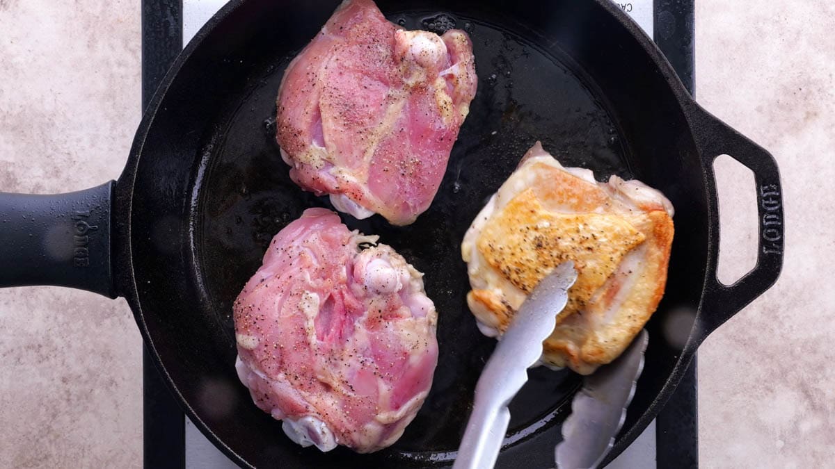 Flipping chicken thighs in a skillet.