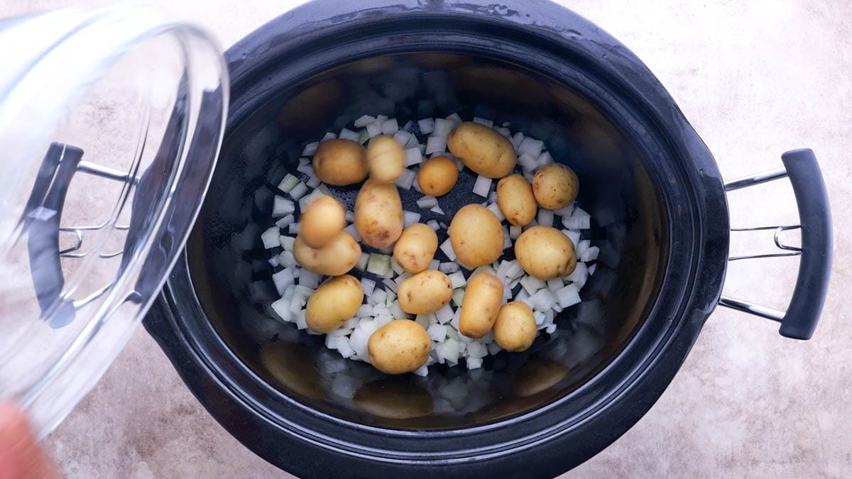 Crock pot with onions and potatoes in the bottom.