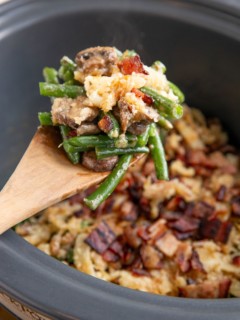 Wooden spoon scooping some green bean casserole out of the slow cooker.