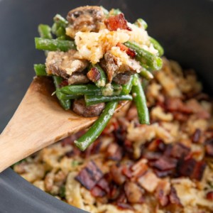Wooden spoon scooping some green bean casserole out of the slow cooker.