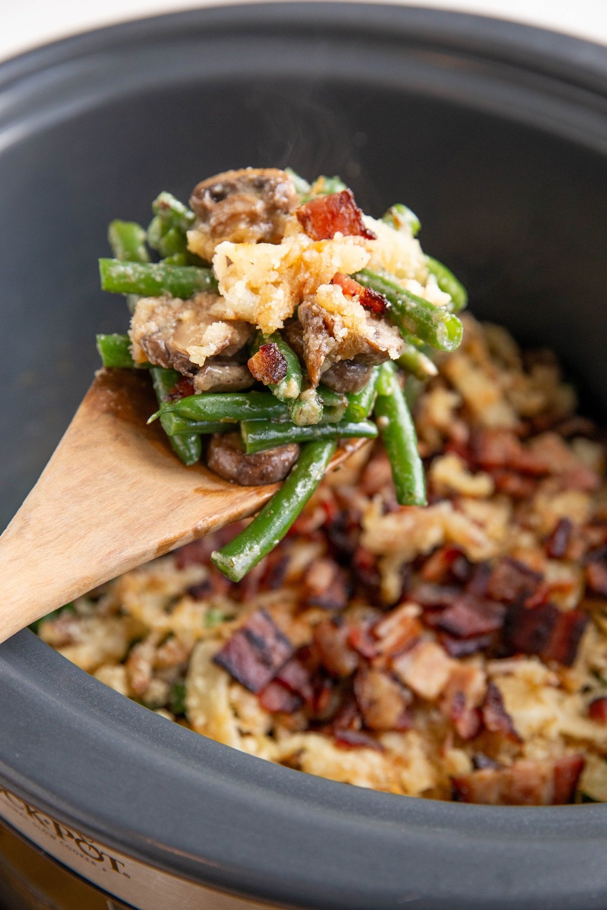 Wooden spoon scooping some green bean casserole out of the slow cooker.