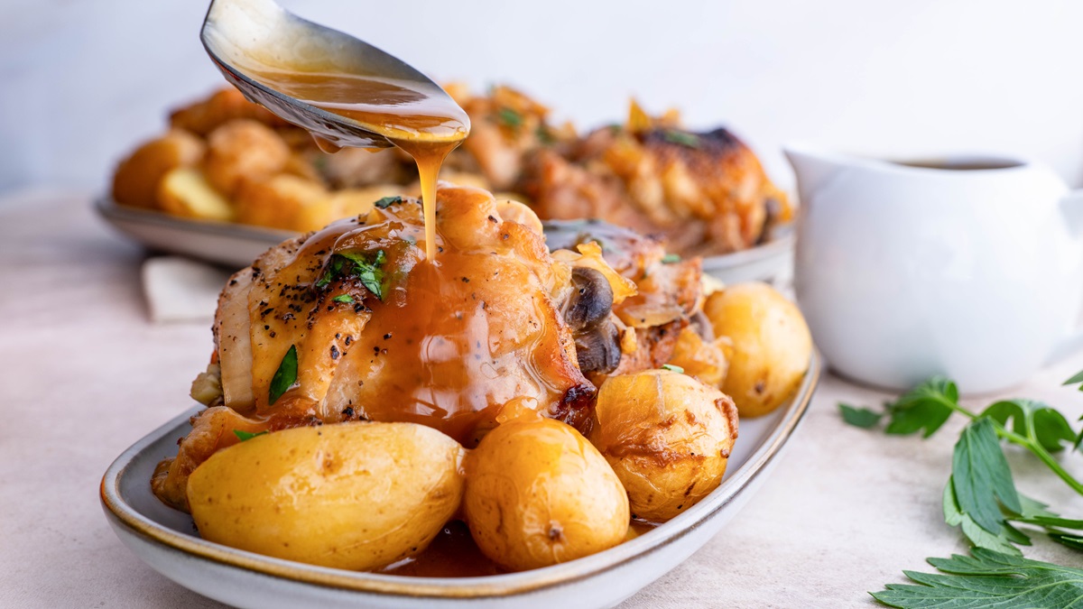 Spoon drizzling juices over chicken and potatoes.