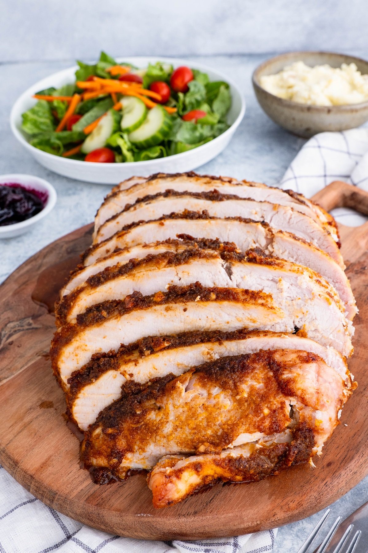 Sliced roast turkey breast on a cutting board with side dishes in the background.