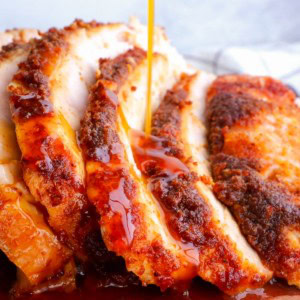 Close up of turkey drippings being poured over sliced turkey breast on a cutting board.