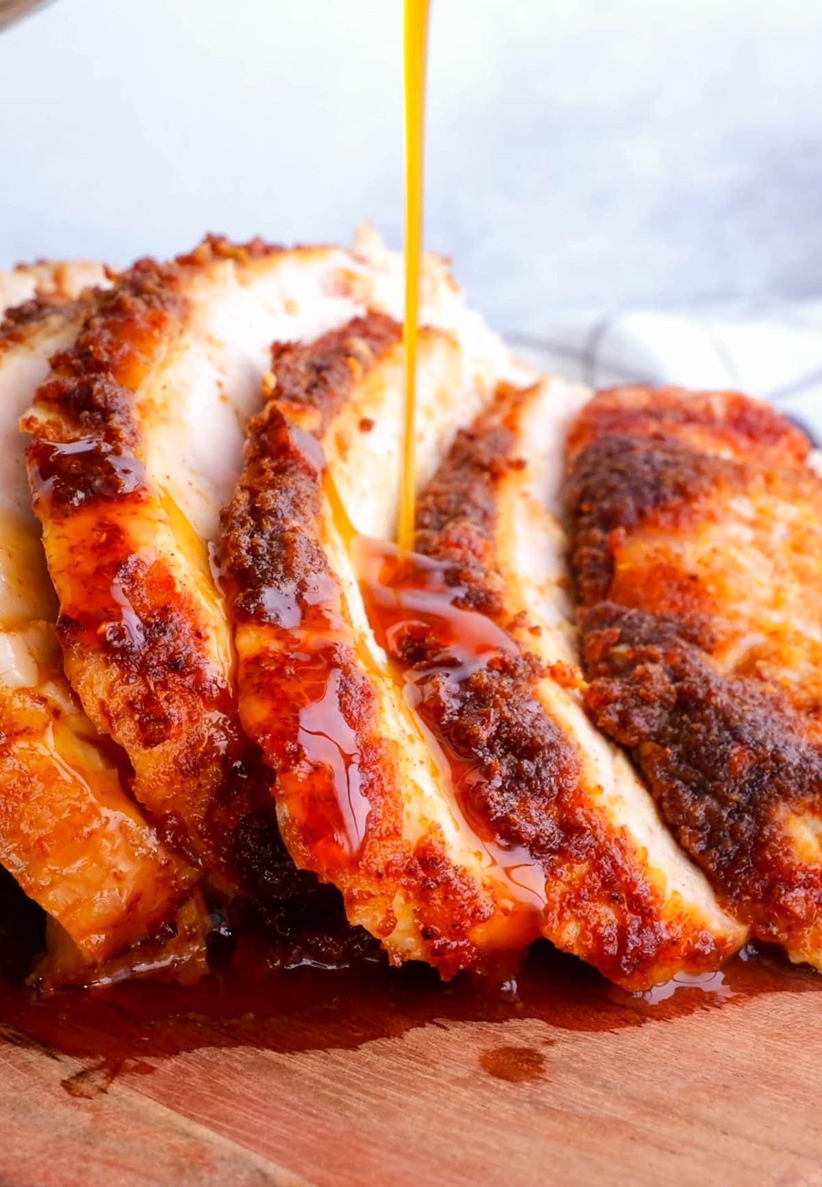 Close up of turkey drippings being poured over sliced turkey breast on a cutting board.