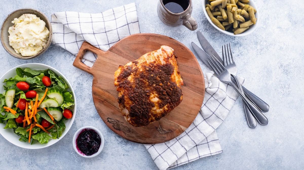 Finished garlic butter turkey breast on a wood cutting board with side dishes to the side.