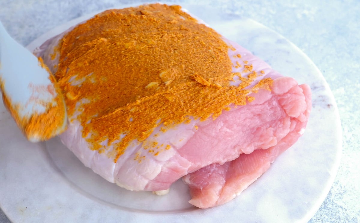 Raw turkey breast being smeared with garlic butter mixture.
