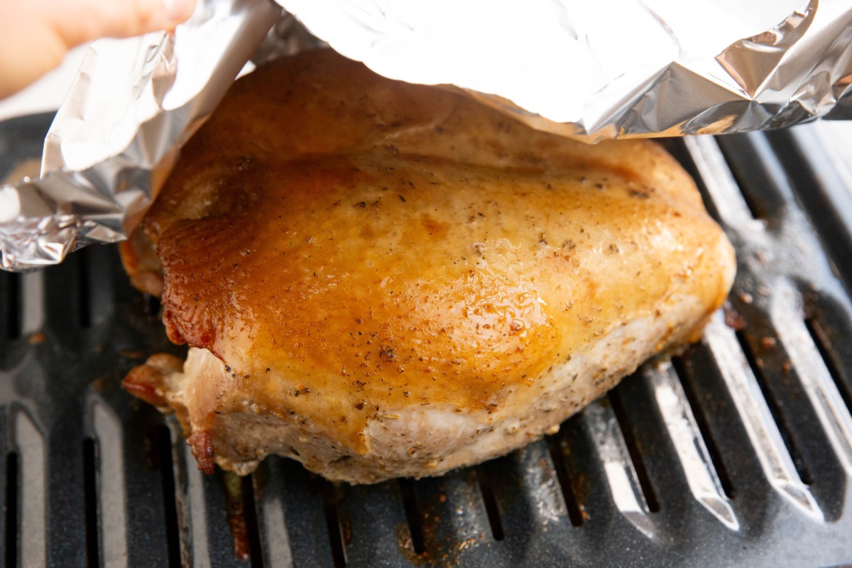 Putting sheet of aluminum foil on top of turkey breast.