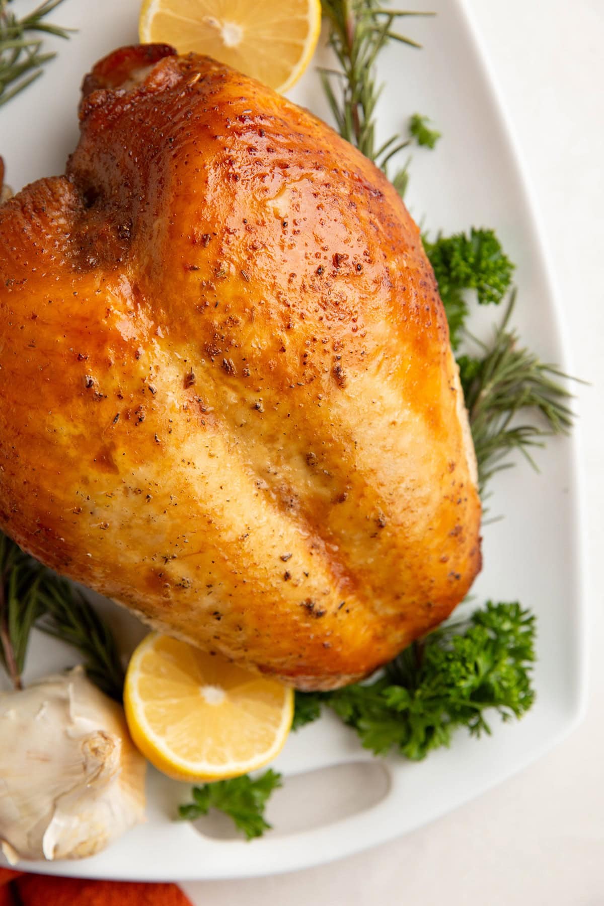 Garlic Herb Roasted Turkey breast on a serving plate with fresh herbs and lemons all around.