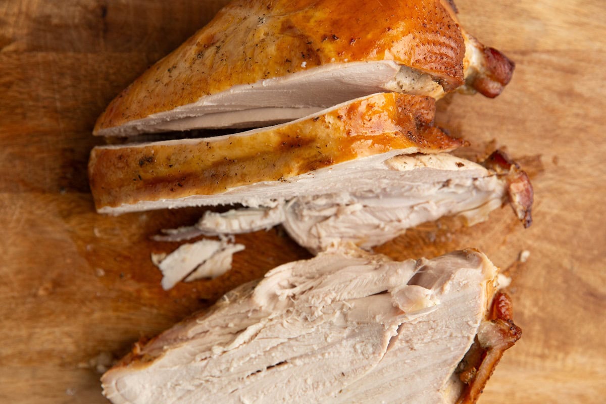 Wooden cutting board with bone-in turkey breast being carved.