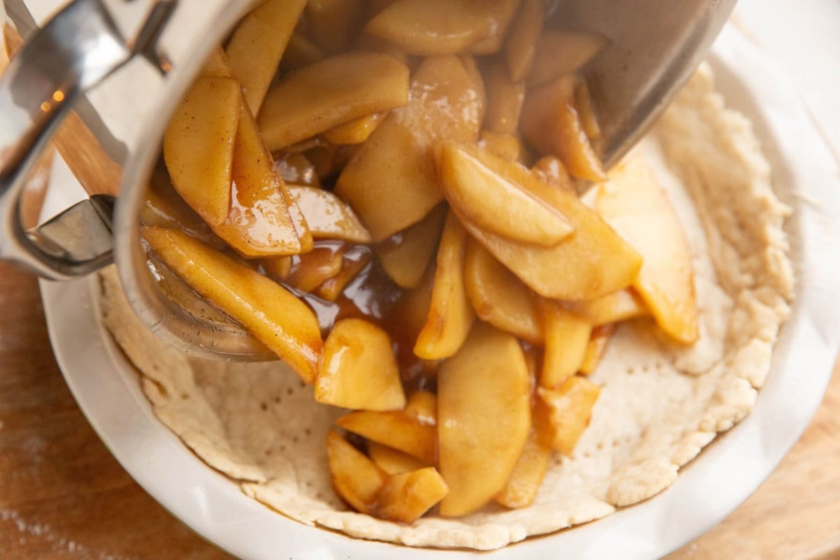 Pouring apple mixture into a prepared pie crust.