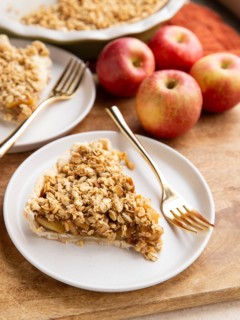 Two slices of gluten-free apple pie on white plates with apples in the background.