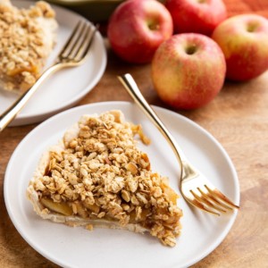 Two slices of gluten-free apple pie on white plates with apples in the background.