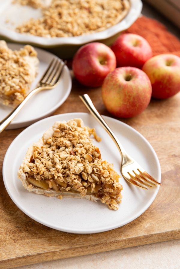 Two slices of gluten-free apple pie on white plates with apples in the background.