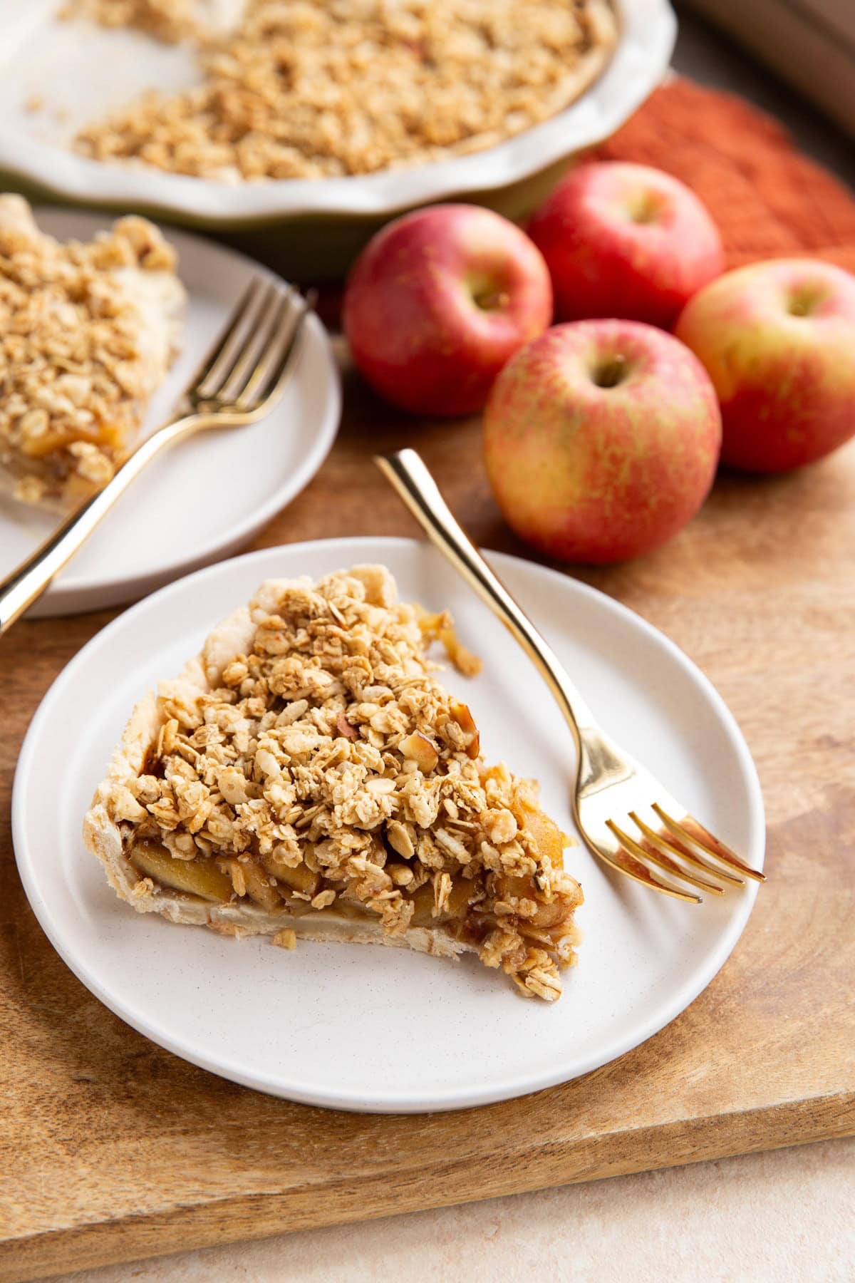 Two slices of gluten-free apple pie on white plates with apples in the background.