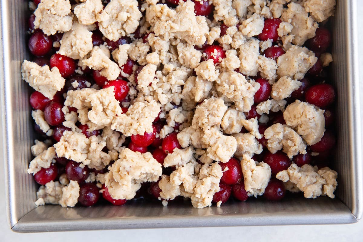 Baking dish with cranberry filling and crumble topping on top, ready to bake