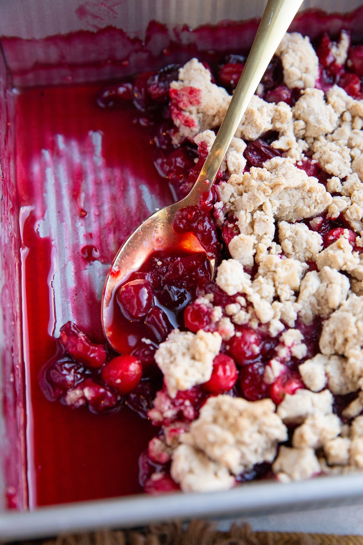 Baking dish of gluten-free cranberry crumble with a gold spoon, scooping and serving.