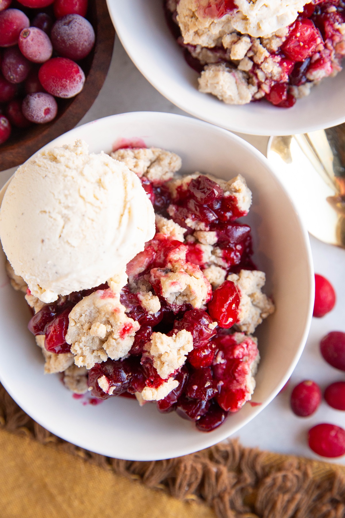 Two white bowls of cranberry crumble with scoops of ice cream on top.
