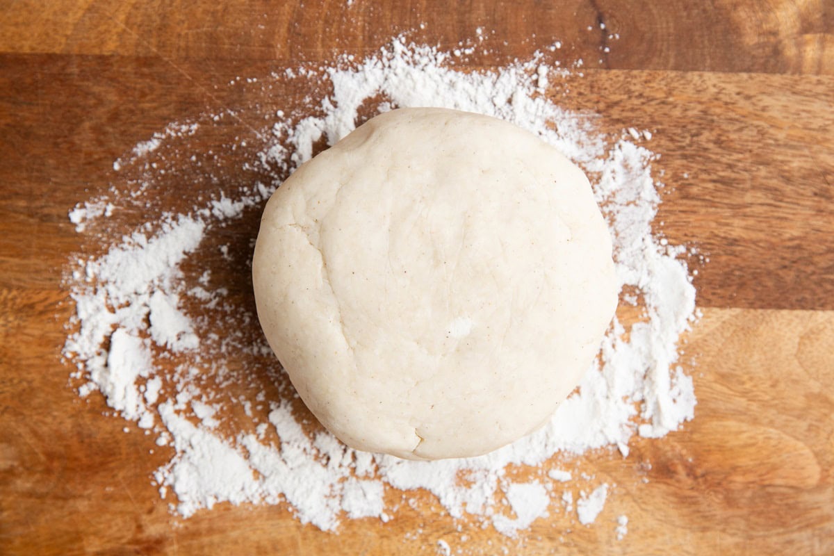 Floured cutting board with dough disc in the center, ready to be rolled out.