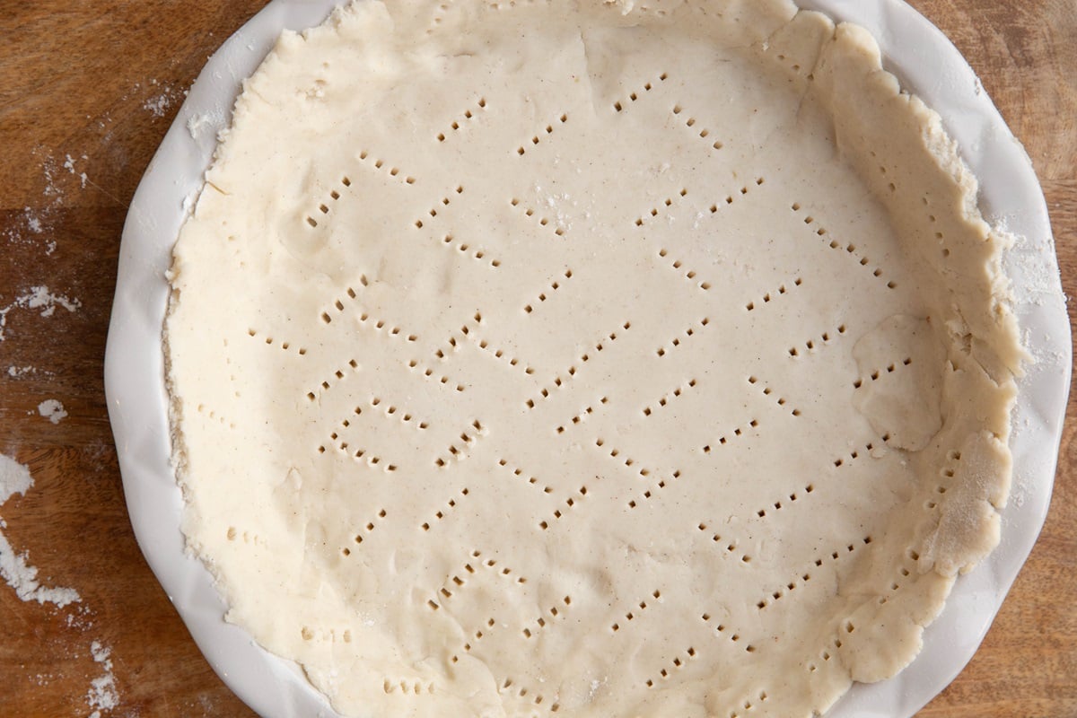 Pie dough poked with many holes in a pie pan.
