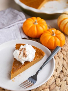 White plate with a slice of crustless pumpkin pie with whipped cream on top and the rest of the pie in the background.