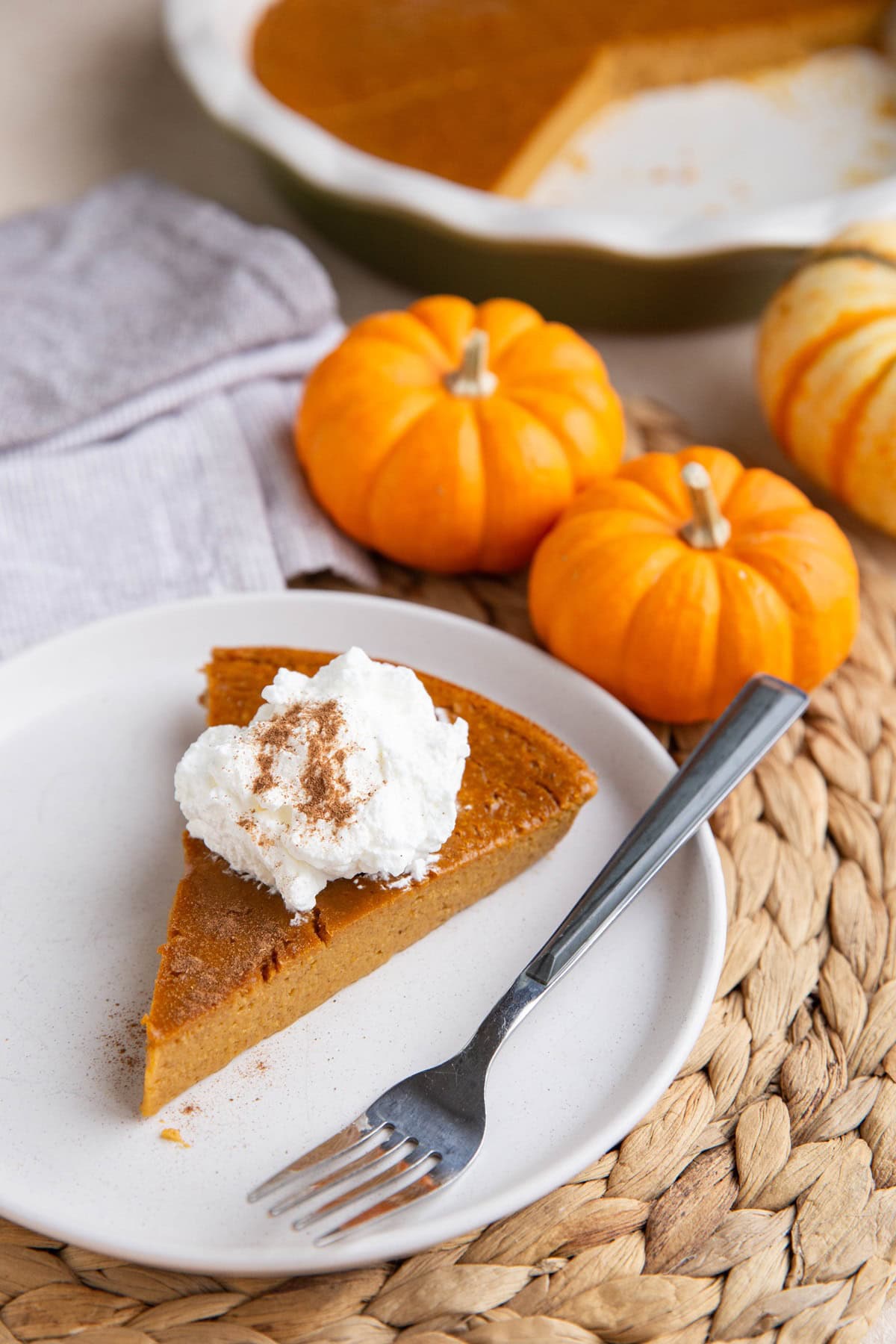 White plate with a slice of crustless pumpkin pie with whipped cream on top and the rest of the pie in the background.