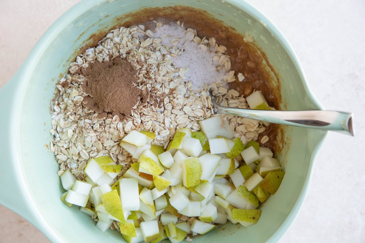 Oats, chopped pear, cinnamon and salt on top of wet ingredients in a mixing bowl, ready to be mixed together.