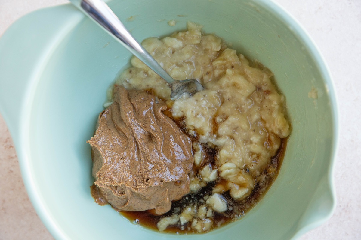Almond butter, mashed banana, pure maple syrup in a mixing bowl, ready to be mixed together.