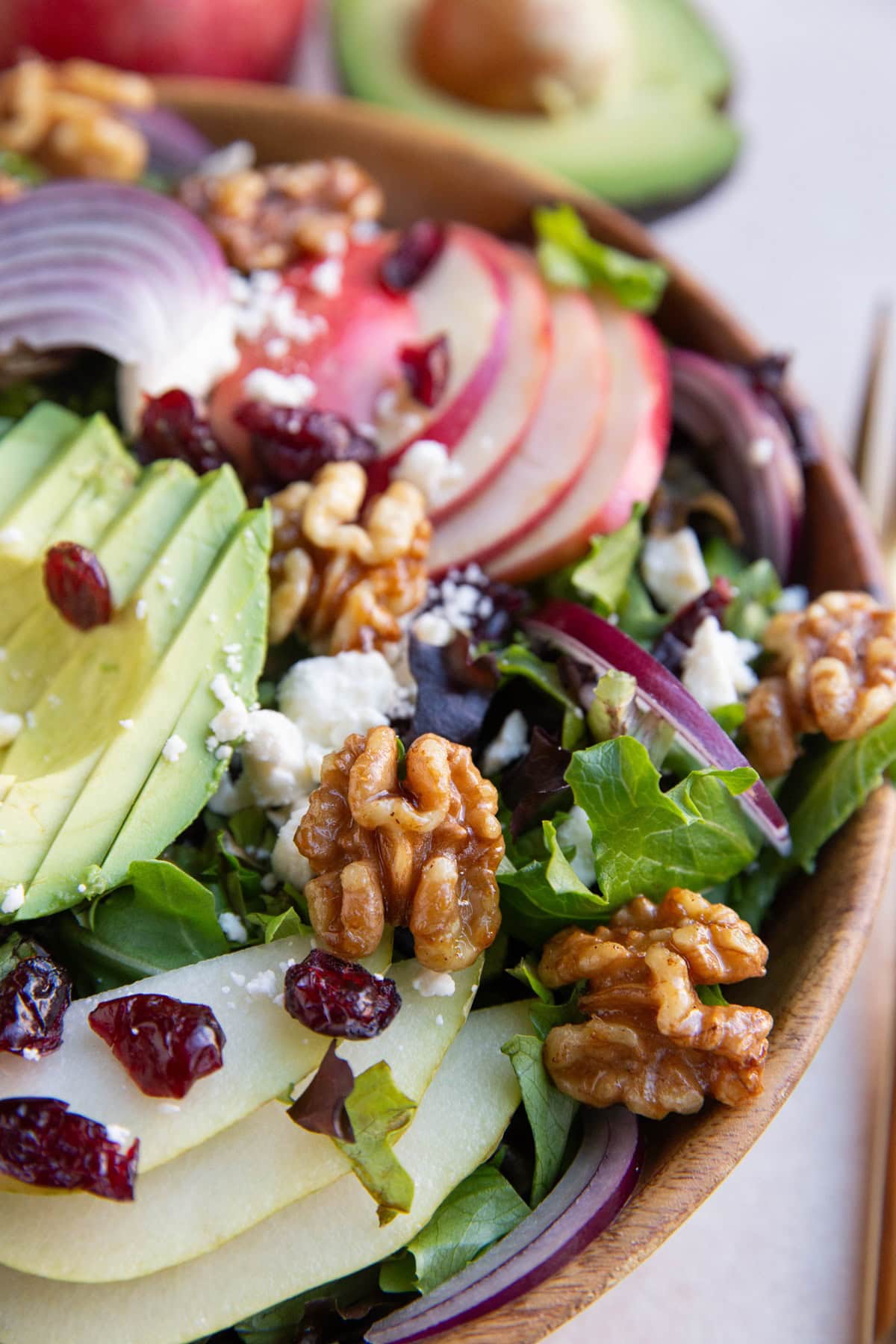 Big wooden bowl of pear apple avocado spinach salad with a gold fork to the side.