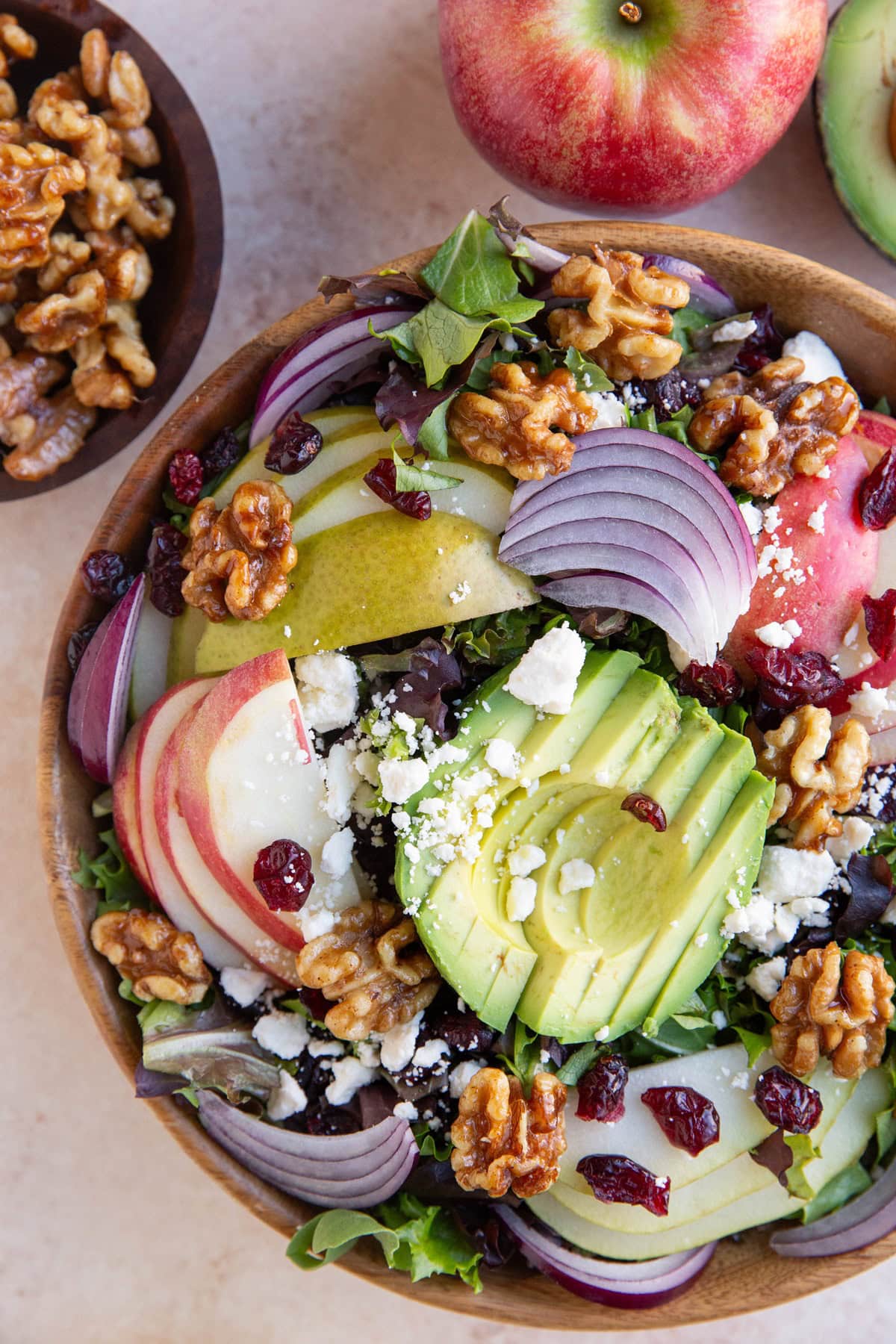 Wooden bowl of salad with avocado, apples, pears and more. A bowl of candied walnuts to the side.