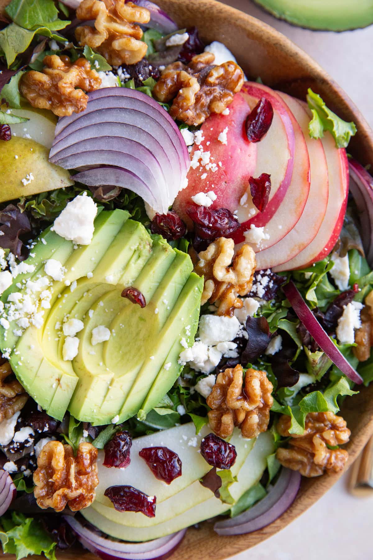 Wood bowl of salad with avocado, pears, apples, red onion, walnuts and feta cheese.