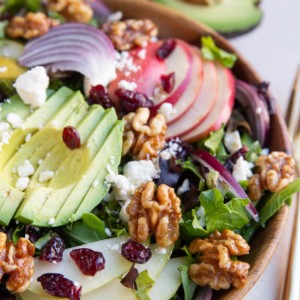 Bowl of salad with pears, apples, walnuts, etc and fresh apple and avocado in the background.