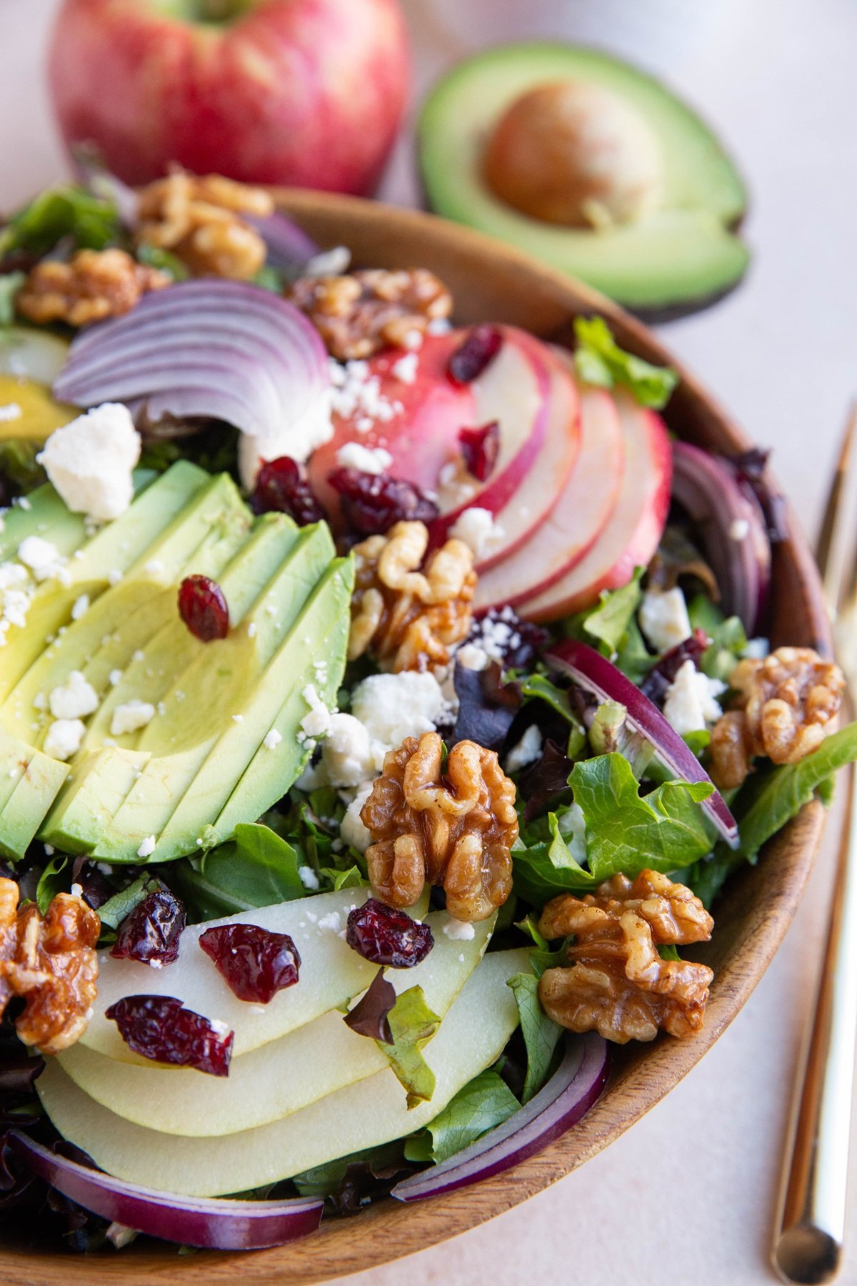 Bowl of salad with pears, apples, walnuts, etc and fresh apple and avocado in the background.