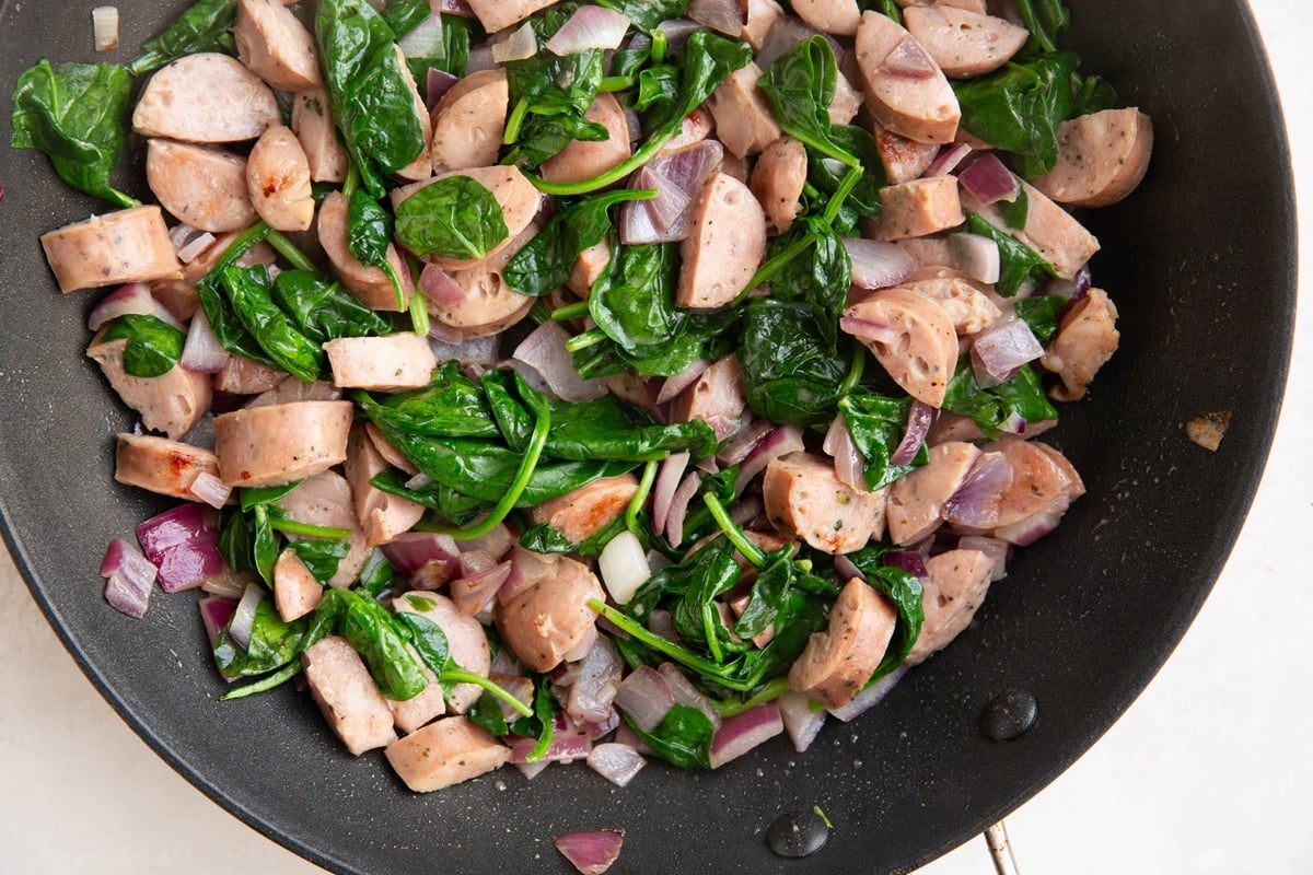 Sausage, onion, spinach cooking in a skillet