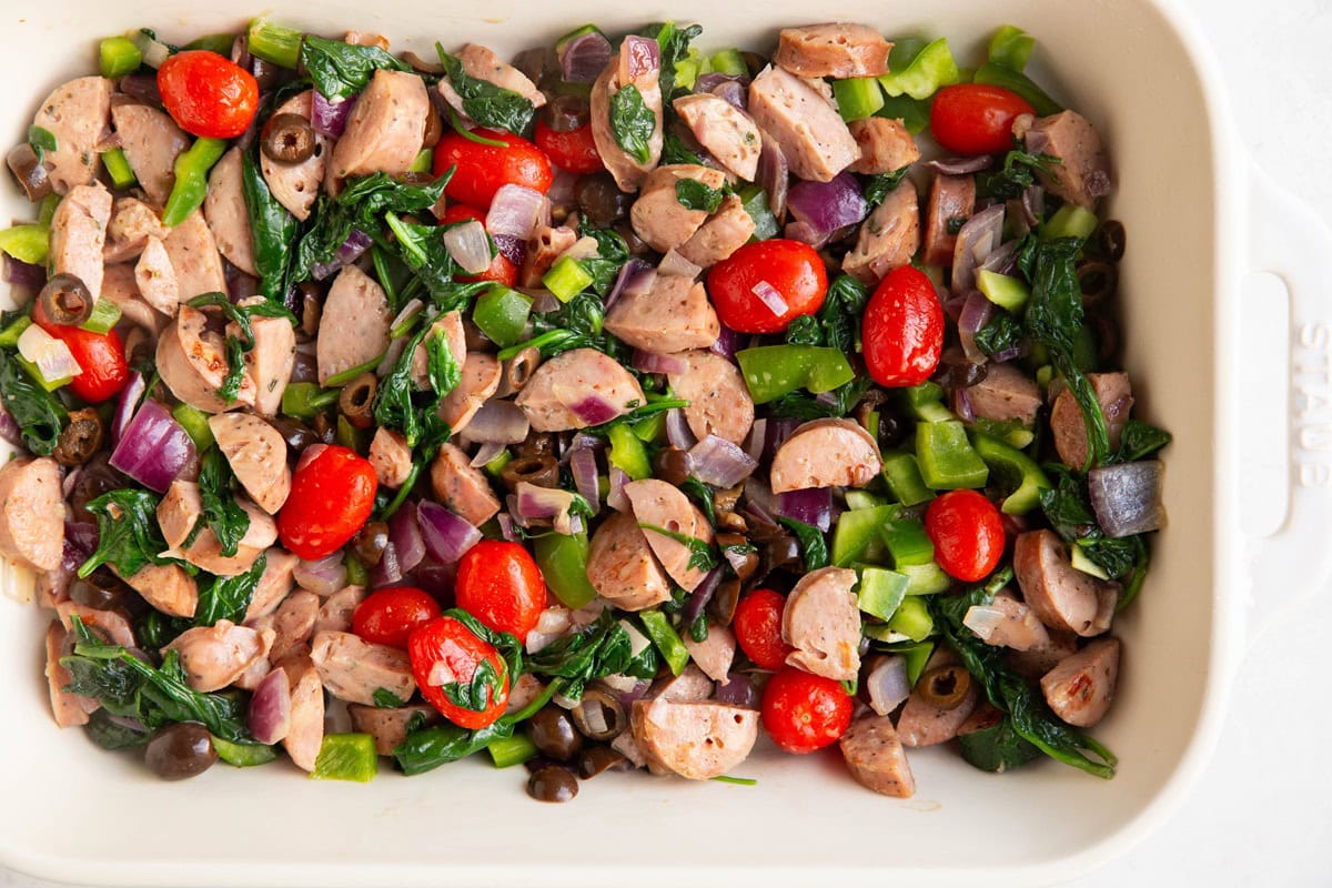 Sausage, onion, bell peppers, tomatoes, olives and garlic in a casserole dish.