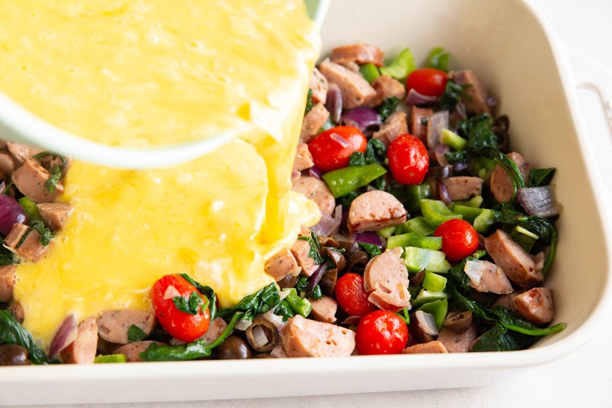 Pouring the egg mixture over everything in the casserole dish.