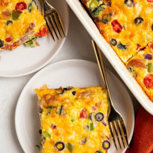 Slices of sausage egg bake on white plates with the casserole dish to the side, ready to serve.