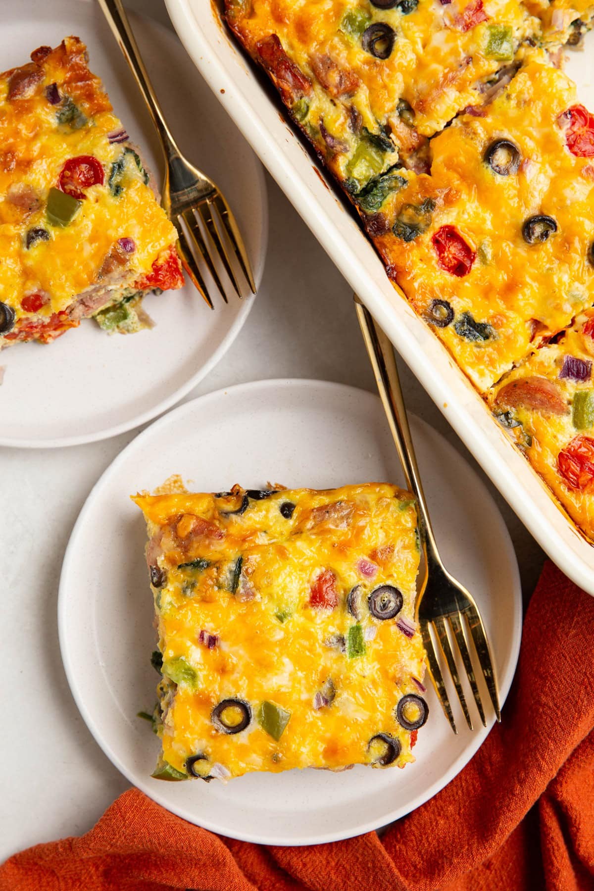 Slices of sausage egg bake on white plates with the casserole dish to the side, ready to serve.