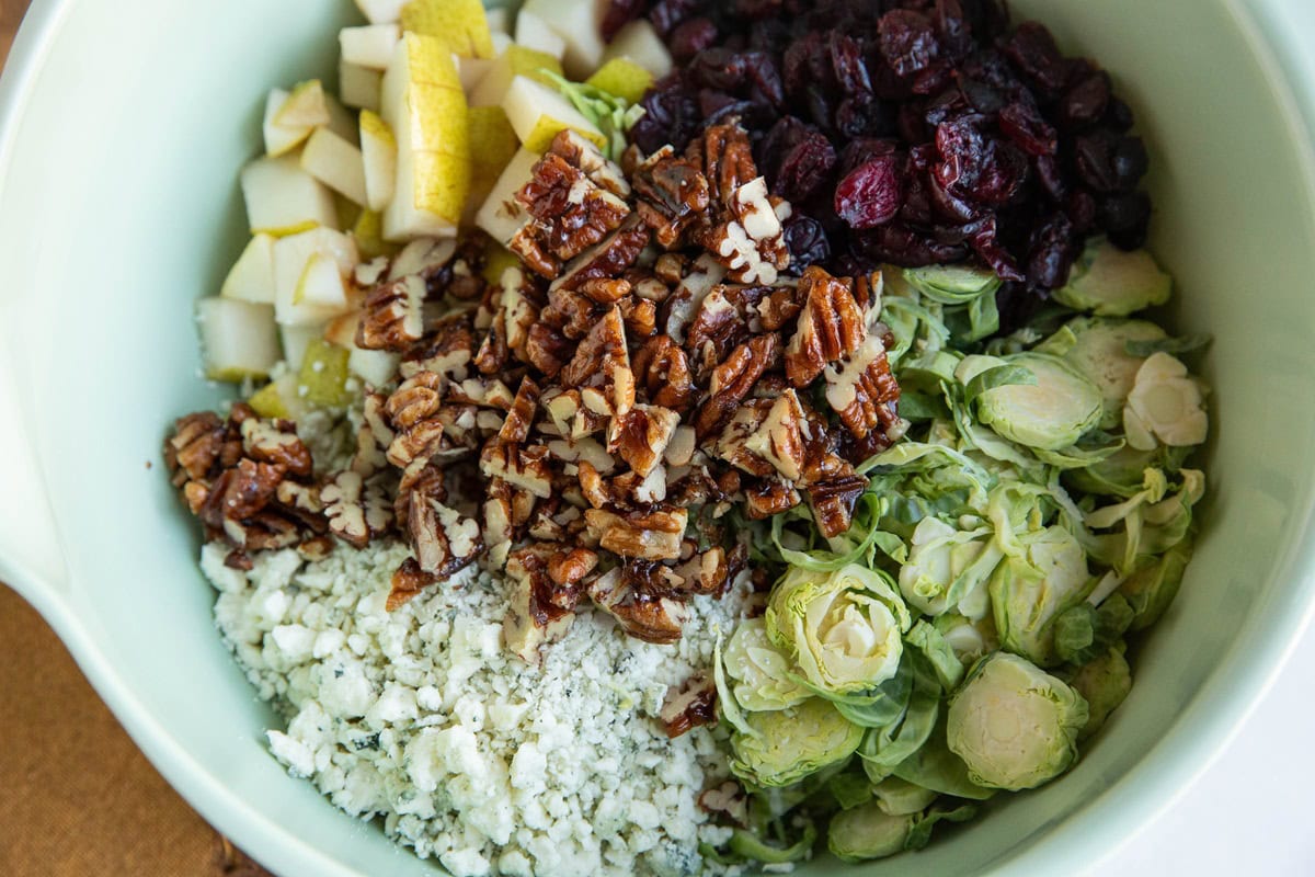 Green bowl with shredded brussel sprout salad ingredients inside, ready to be mixed up.