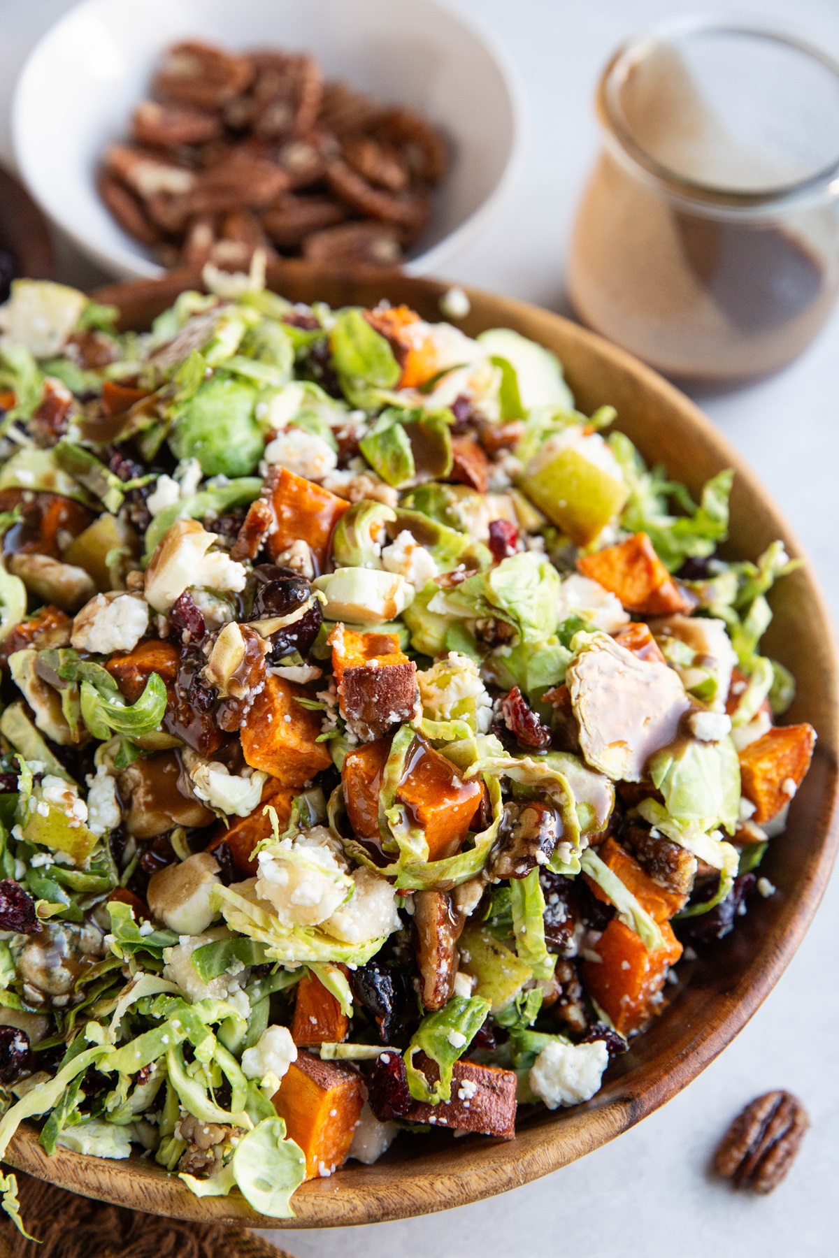 Bowl of shaved brussel sprout salad with all sorts of goodies inside and balsamic vinaigrette in the background.
