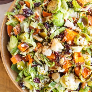 Big bowl of brussel sprout salad with sweet potato, blue cheese, dried cranberries, pears, and more.